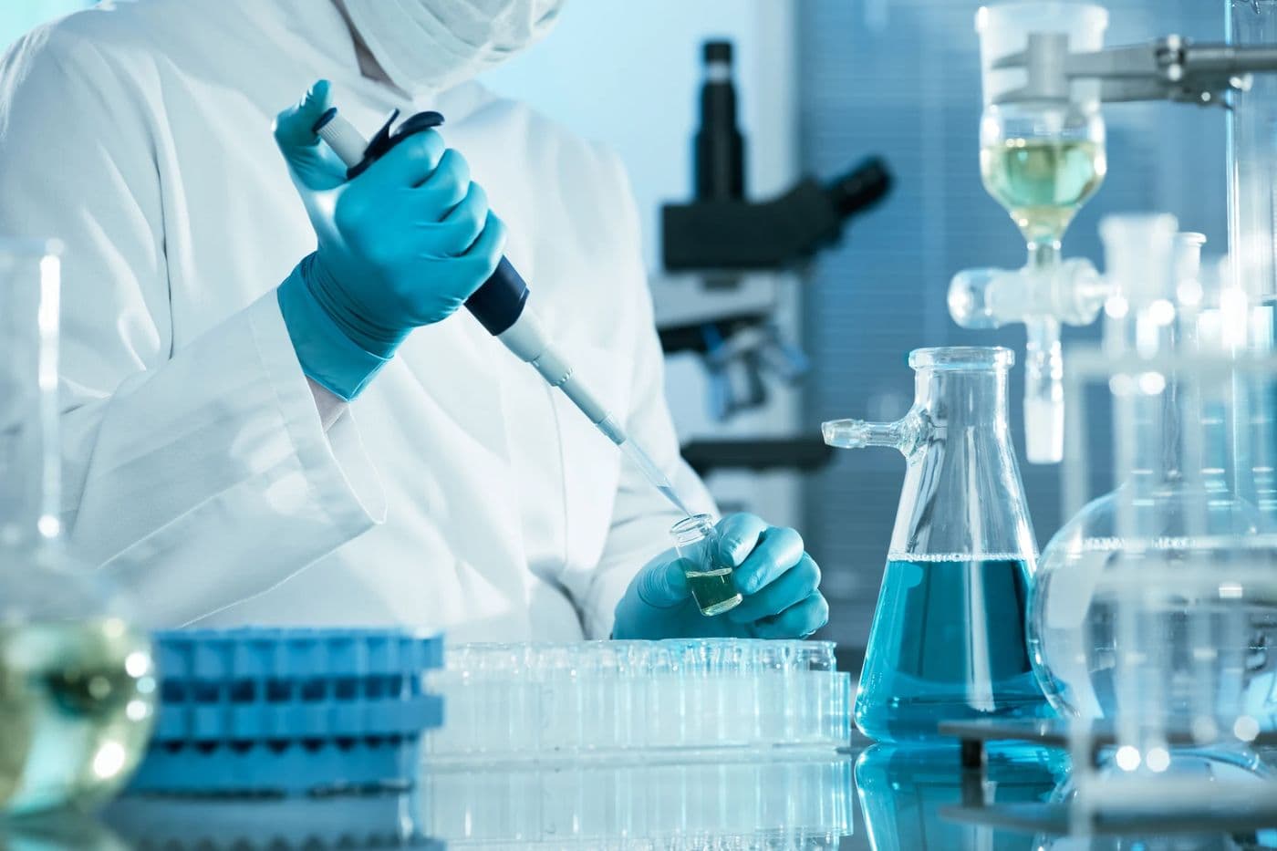 A scientist pipetting a sample beside flasks of blue solution in the Rameda laboratory